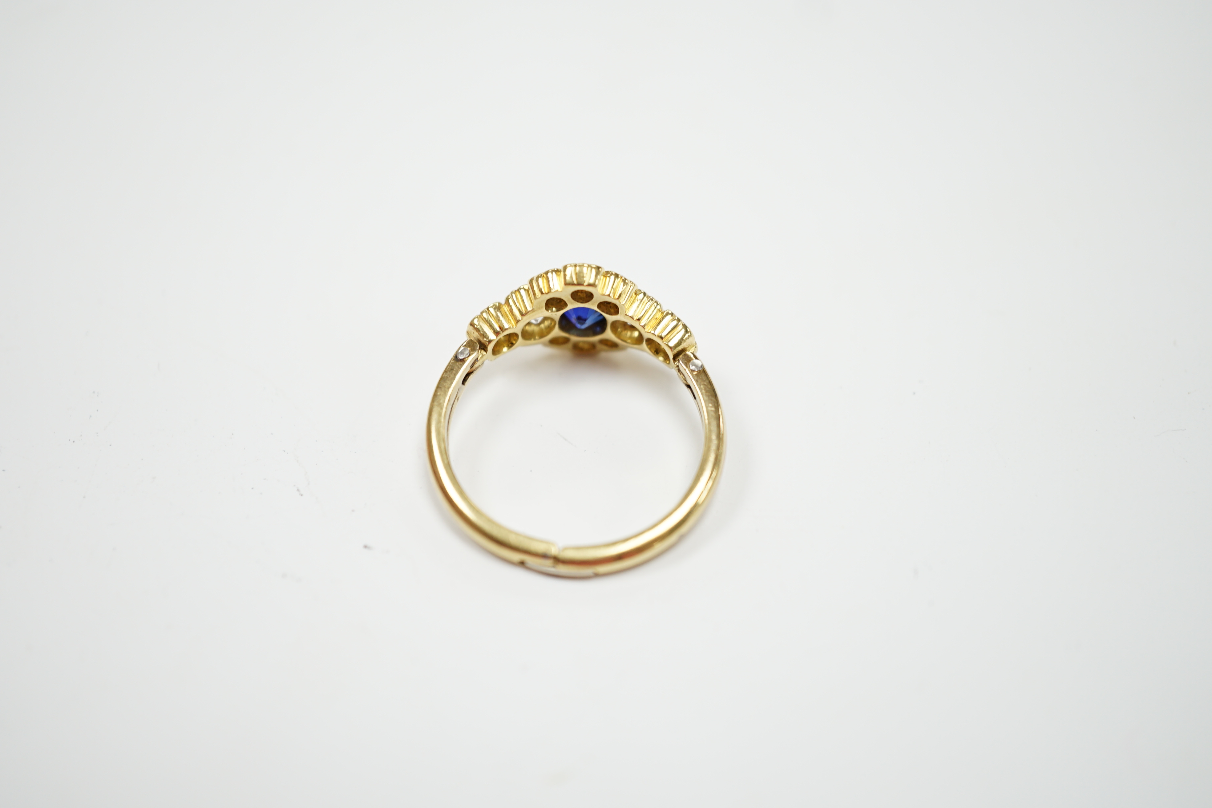 A modern yellow metal, synthetic sapphire and diamond set flower head cluster ring, with hinged shank, size U, gross weight 5.1 grams.